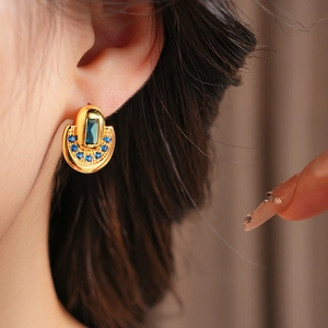 Détail de boucle d'oreille vintage en forme de U dorée avec zircons bleus