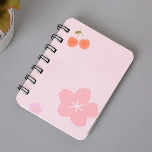 Detail of pink A7 spiral notebook with cherry patterns and cute Chinese text on gray desk