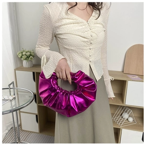 Nahaufnahme der metallisch lila Plissee-Handtasche mit Ringgriff in modernem Ambiente