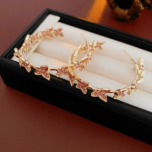 Gros plan de boucles d'oreilles créoles papillon dorées avec cristaux roses dans un écrin