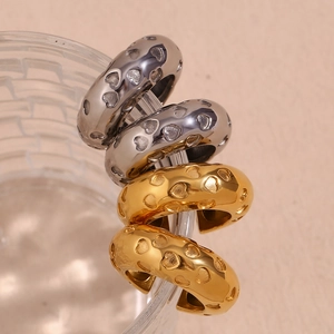 Detail of gold and silver heart-embossed stainless steel clip earrings on glass