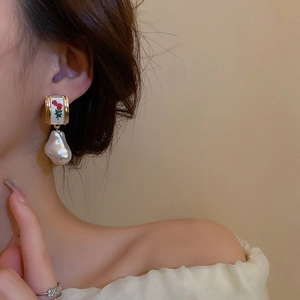 Close-up of vintage earrings with rose motif and irregular pearl pendant on model