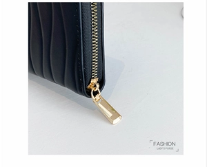 Detail of golden metal zipper and wave quilted texture on a black long leather wallet