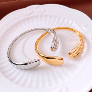 Detailed view of 18K gold and silver plated open bangles on a white ceramic tray