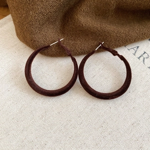 Vue rapprochée des boucles d'oreilles créoles en velours marron sur lin beige