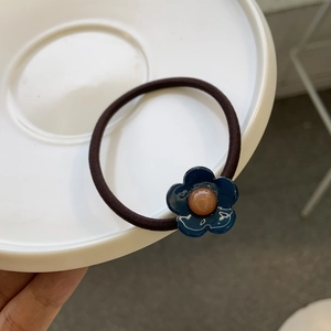 Détail d'un élastique à cheveux marron avec fleur bleue et centre orange dans un plateau blanc