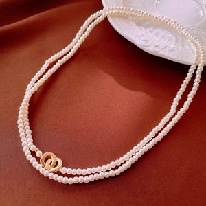 Elegant double-layer pearl necklace with golden interlocking rings on a red velvet background