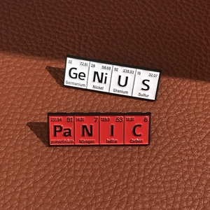 Creative chemistry element pins GeNiUS and PaNIC on premium brown leather surface