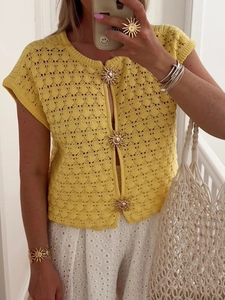 Detail of yellow knit cardigan featuring hollow-out patterns and gold sun-shaped buttons