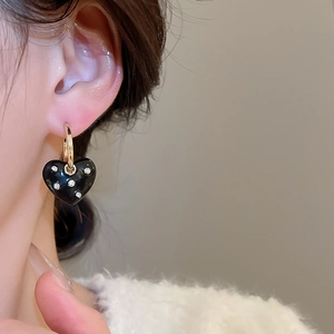 Close-up of black heart earrings with gold hoops and small sparkling diamonds