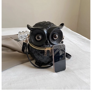 Detail view of owl-shaped crossbody bag with gold zippers and scale texture with phone scale