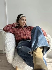 Dettaglio camicia a quadri rossa abbinata a jeans strappati e stivaletti beige