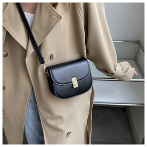 Classic black leather saddle bag with gold hardware worn over a khaki trench coat