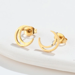 Detail of minimalist gold crescent moon stud earrings on white textured stone surface