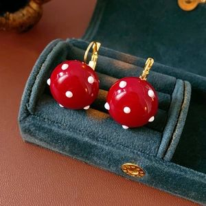Close-up of red mushroom earrings with white polka dots in a green velvet jewelry box