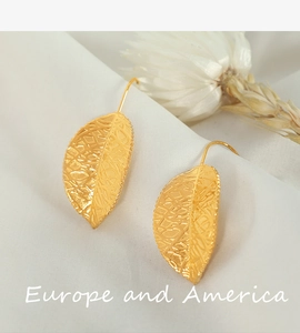 Close-up of gold-plated leaf earrings with detailed vein texture on white fabric