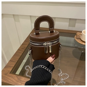 Détail d'un sac cylindrique marron foncé avec chaîne argentée et poignée supérieure