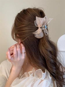 Detail of oversized peach organza mesh bow hair claw clip styled on dark wavy hair