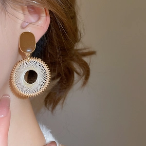 Macro detail of Bohemian woven gold hoop earrings with white thread and brown studs