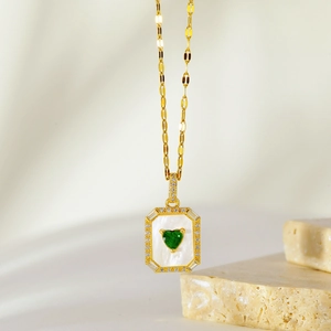 Detailed close-up of a gold heart pendant with green gemstone on a marble background