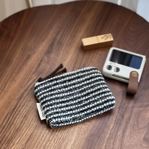 Close-up of black and white tweed mini pouch with zipper on a dark wood table