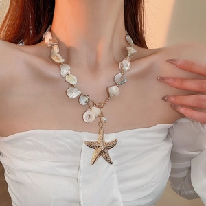 Detail of beach style necklace featuring golden starfish, white shells and pearls on neck