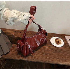 Detail view of burgundy shiny leather handbag with silver hardware on a wooden table