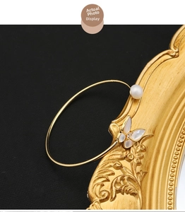 Detail of gold butterfly bracelet with natural pearl and zircon on black backdrop