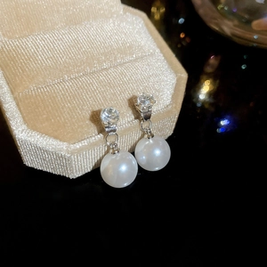 Macro shot of silver pearl earrings with zircon inlay on beige velvet display stand