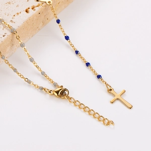 Detail of gold Y-necklace with cross pendant and blue grey beads on stone prop