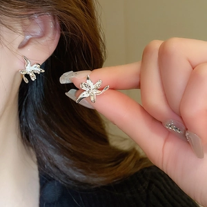Detailed view of silver lily flower stud earrings on ear showing delicate metal petal design
