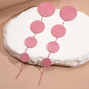 Close-up of pink geometric tassel earrings with hammered texture on white stone
