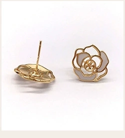 Detailed view of gold rose earrings with white enamel petals in a studio shot