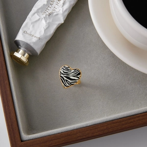 Detailed close-up of heart-shaped 18K gold ring with zebra print on grey velvet tray