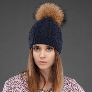 Close-up of a dark blue cable knit beanie featuring a fluffy brown faux fur pom pom top