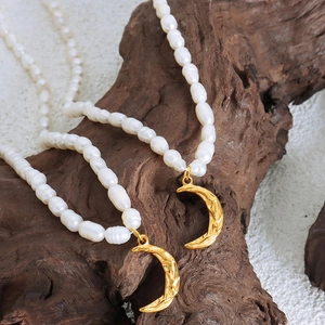 French style pearl necklace with gold moon pendant displayed on a dark wood background