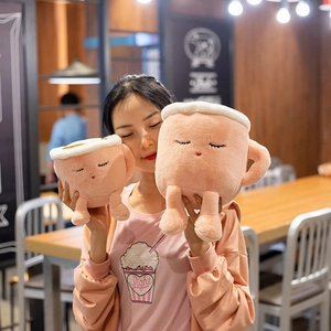 Cute pink plush latte coffee cup toys in two sizes held by a model in a warm cafe