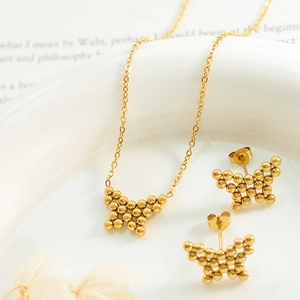 Golden butterfly jewelry set with steel beads necklace and earrings in a ceramic bowl