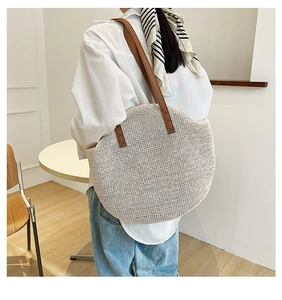Close-up of a large beige straw woven shoulder bag with brown leather straps for travel