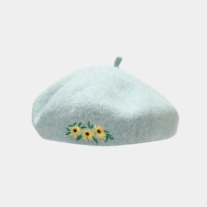 Close-up of three sunflower embroidery details on a light blue wool beret hat