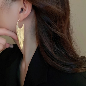 Detail view of a long gold tassel earring with sleek metallic fringe on a female model