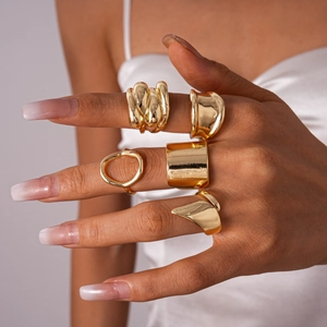 Five-piece set of geometric irregular gold metal rings worn by a model on white satin