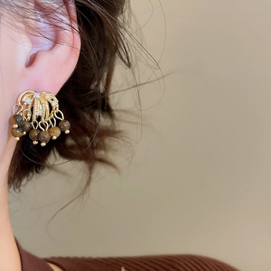 Close-up of golden tassel earrings with brown beads and zircon stones on a model