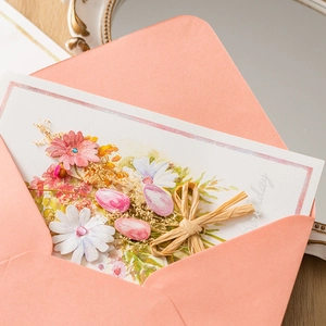 Handmade dried flower greeting card with pink envelope on a rustic wooden desk