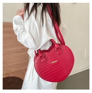 Détail d'un sac à main rouge en forme de cœur avec texture crocodile et logo doré