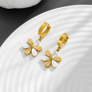 Close-up of gold flower earrings with white shell petals and matte finish on a tray
