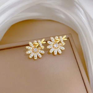 Macro detail of gold flower stud earrings with sparkling white zircons on silk fabric