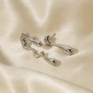 Close-up of asymmetric silver teardrop and wavy stud earrings on champagne silk fabric