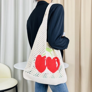 White knitted tote bag with red cherry pattern shown on shoulder in a minimalist room