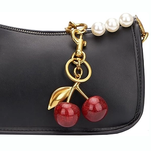 Porte-clés cerise 3D avec matériel doré et perles sur un sac à main en cuir noir